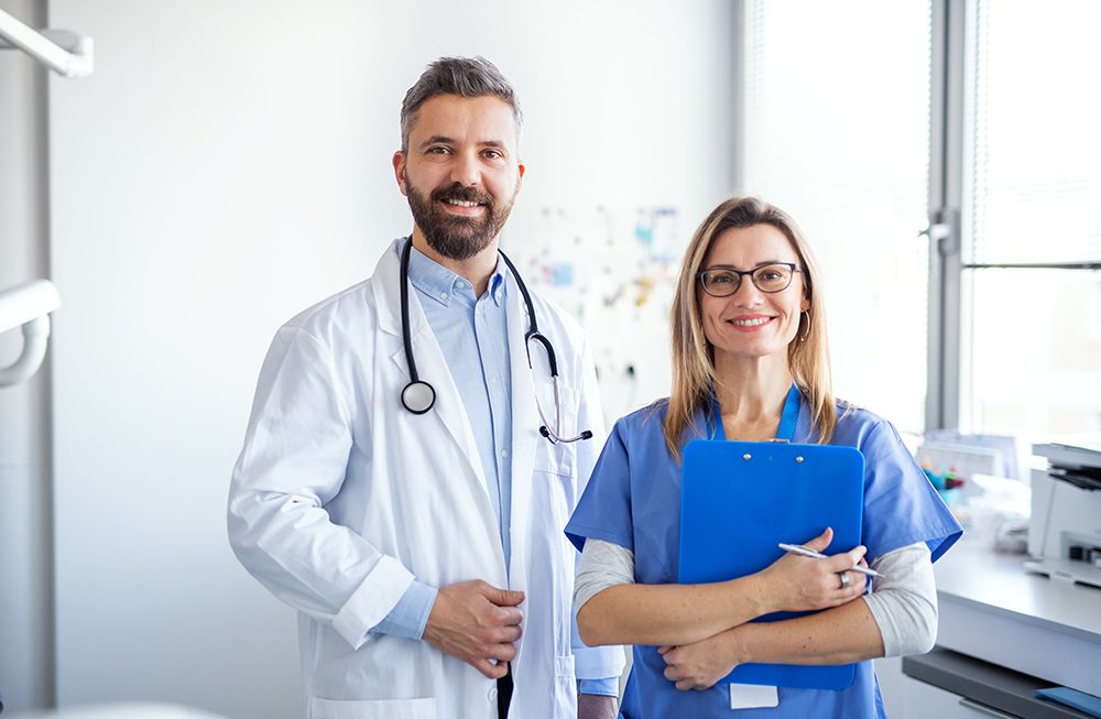 A dentist with dental assistant in modern dental surgery, looking at camera.